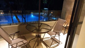 Ein verglaster Balkon mit einem runden Tisch und vier Stühlen, mit Blick auf einen Poolbereich.