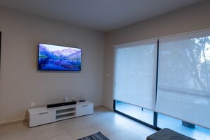 Ein modernes Wohnzimmer mit einem an der Wand befestigten Flachbildfernseher, einer Schiebetür zum Balkon und einer schlichten Unterhaltungseinrichtung.