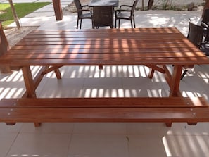 Ein Holztisch für ein Picknick mit Bänken, umgeben von Stühlen und einem kleinen Tisch.