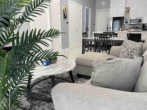 Ein modernes Wohnzimmer mit einem runden Tisch, einer Couch und einer Topfpflanze.