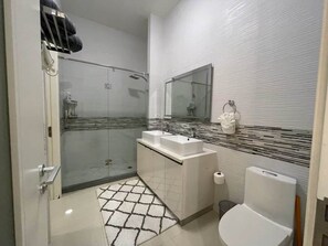 Uma casa de banho moderna com cabine de duche em vidro, uma sanita e um lavatório branco com espelho por cima.