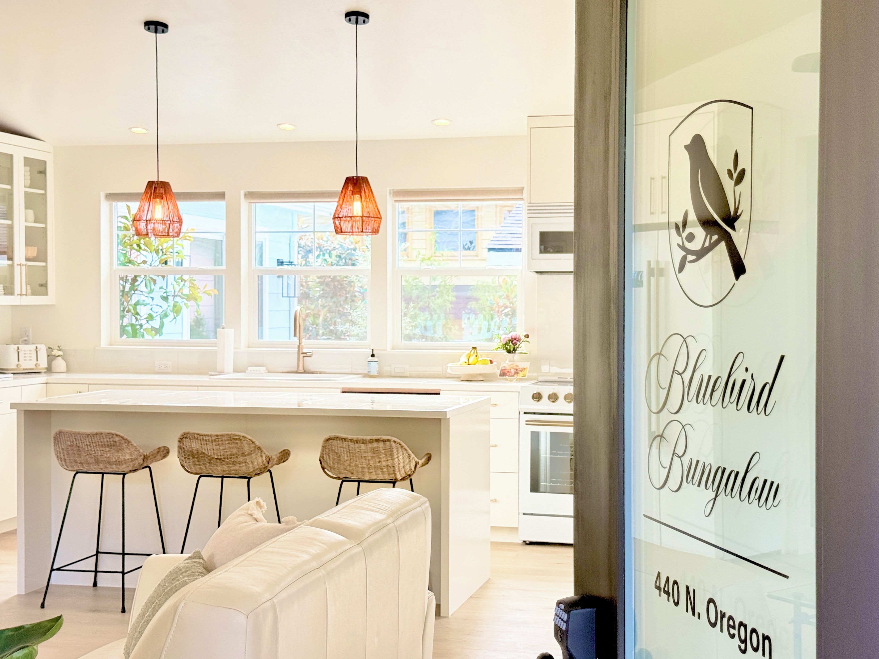 A modern kitchen with pendant lights, a central island, and a view of greenery outside.
