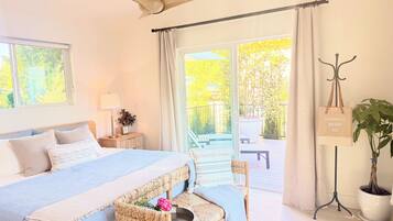 A bedroom with a bed, bedside table, lamp, potted plant, and a view of the outdoors.