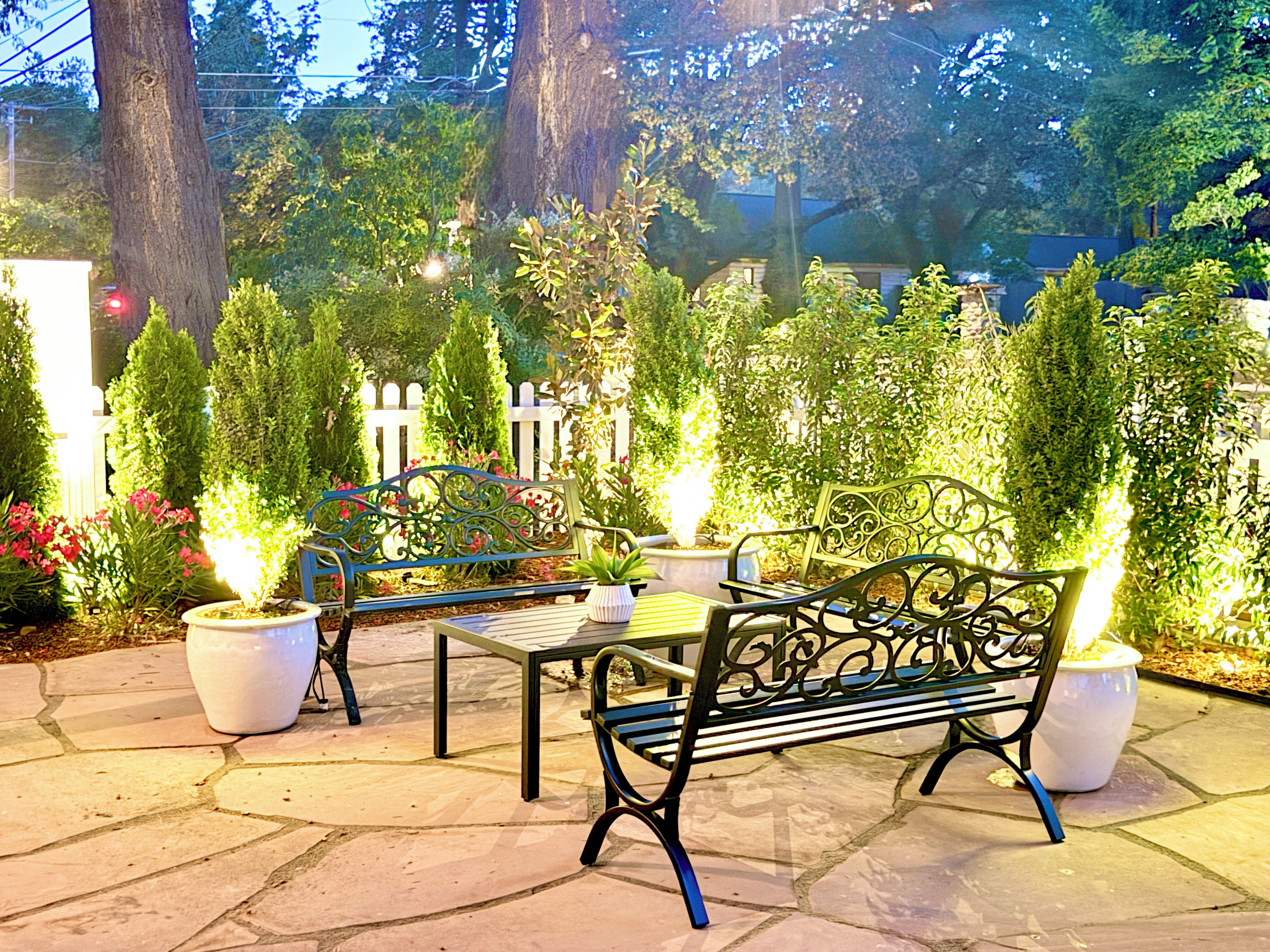 Un espace extérieur aménagé avec deux bancs en métal, des plantes en pot et une clôture blanche en bois.