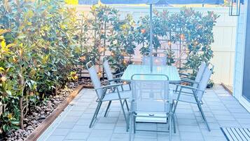 An outdoor patio with a table and chairs, surrounded by plants and a fence.