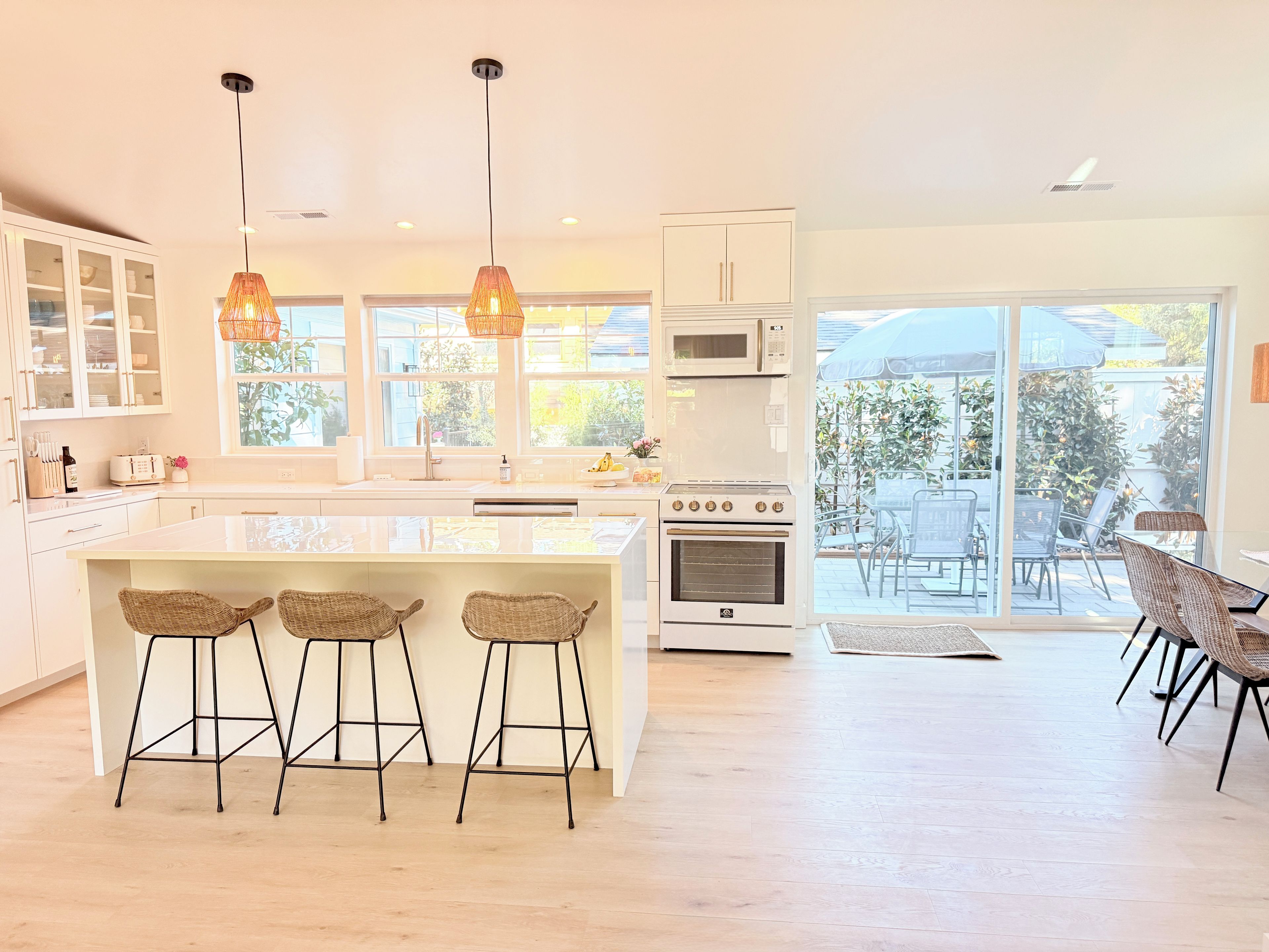 A modern kitchen with a central island, bar stools, and a dining area with outdoor seating.