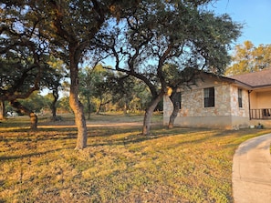A stone building with a porch, surrounded by trees and grass. - Quiet oak-lined retreat in Garden Ridge - 4BR home (Garden Ridge)