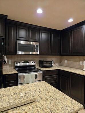 A kitchen with dark wood cabinets, stainless steel appliances, granite countertops, and recessed ceiling lights. - Quiet oak-lined retreat in Garden Ridge - 4BR home (Garden Ridge)