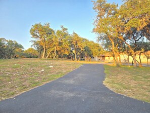 A paved pathway leading to a building with a stone facade, surrounded by trees with autumn foliage. - Quiet oak-lined retreat in Garden Ridge - 4BR home (Garden Ridge)