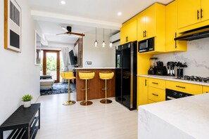 A modern kitchen with yellow cabinets, a black refrigerator, and a gas stove. There are three bar stools with yellow cushions. - Villa Camila Unit 1: Modern, Central Villa with Tranquil Charm (Cooper Jack Bay Settlement)
