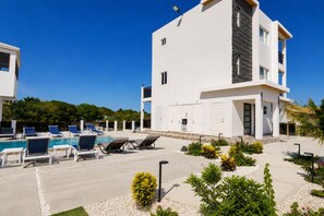 A modern building with a pool area, including lounge chairs and a clear blue sky. - Villa Camila Unit 1: Modern, Central Villa with Tranquil Charm (Cooper Jack Bay Settlement)