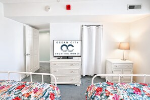 A hotel room with two beds, a television displaying 'Ocean City Vacation Homes,' a white dresser, a lamp, and a door leading to another room. - Golden Sands 1611111 (Ocean City)
