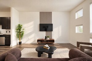A modern living room with a flat-screen TV, a coffee table, and a sofa. - Spacious 1BR | 850 Sq Ft | Design District (Dallas)