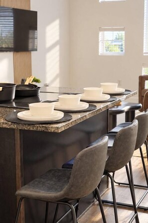 A kitchen with a granite countertop, white plates, and a black range hood. - Spacious 1BR | 850 Sq Ft | Design District (Dallas)