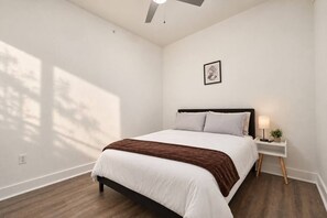 A bedroom with a bed, bedside table, lamp, and a framed picture on the wall. - Spacious 1BR | 850 Sq Ft | Design District (Dallas)