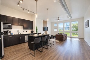 A modern kitchen with dark cabinets, a central island, and bar stools. - Spacious 1BR | 850 Sq Ft | Design District (Dallas)