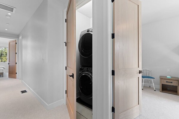 A laundry room with a double washer and dryer, a wooden bench, and a chair. - Downtown WP Creekside Villa 15 | Hot Tub | Bunk Room | Great Views | Discounted Attractions (Winter Park)