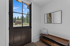 A room with a dark wooden door, a bench with drawers, a white wall, and a window with a view of trees and a building outside. - Downtown WP Creekside Villa 15 | Hot Tub | Bunk Room | Great Views | Discounted Attractions (Winter Park)