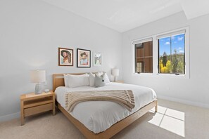 A bedroom with a large bed, two bedside tables, a window with a view of trees, and three framed artworks on the wall. - Downtown WP Creekside Villa 15 | Hot Tub | Bunk Room | Great Views | Discounted Attractions (Winter Park)