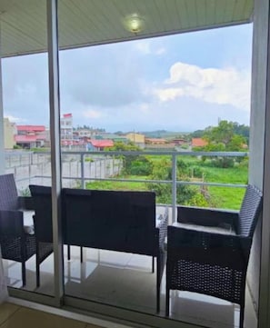 A balcony with a glass door, two chairs, and a view of a cityscape with buildings and greenery. - Costa Rica explorer  (Grecia)
