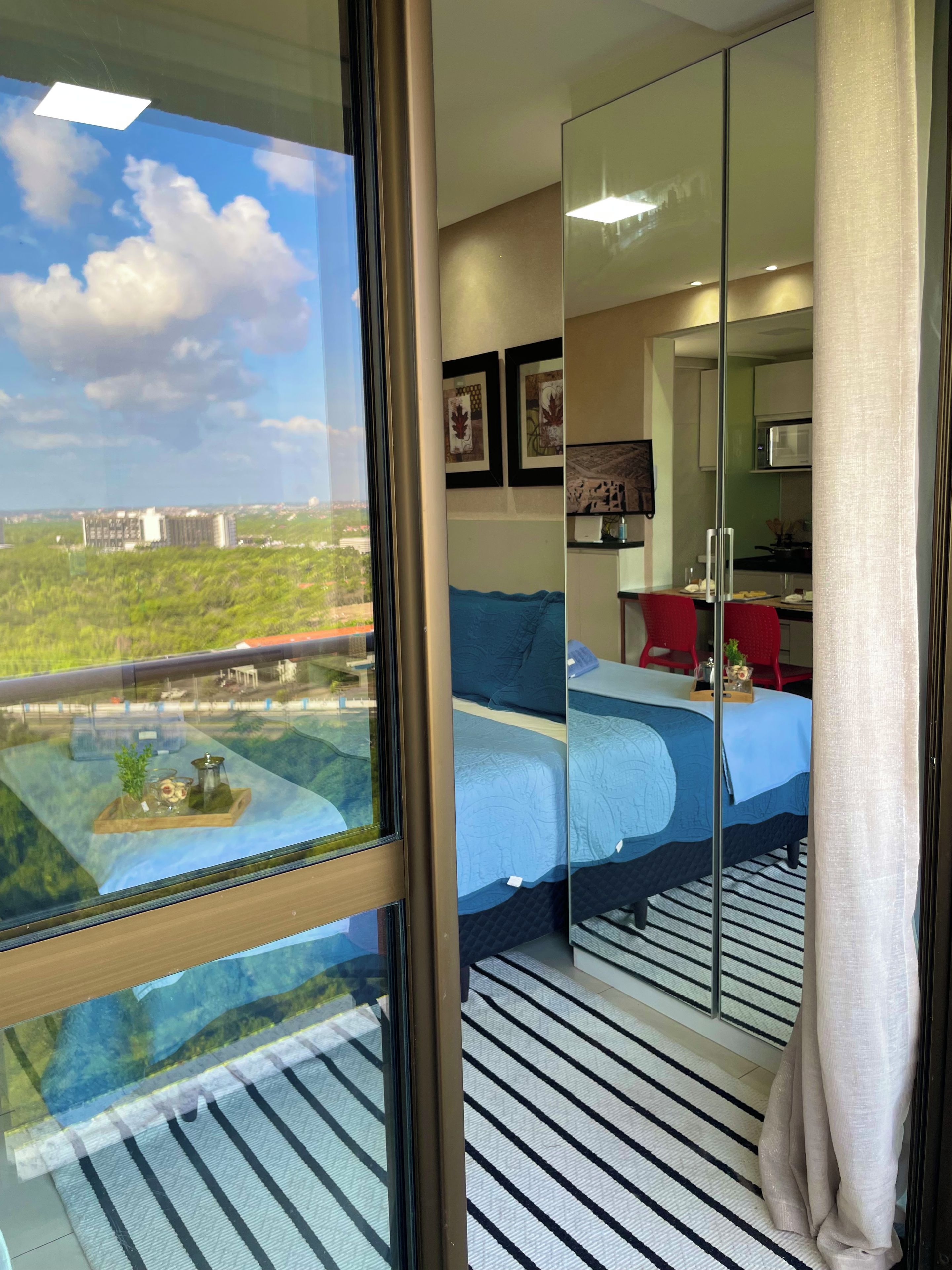 Une chambre d’hôtel avec une grande fenêtre, un lit, un bureau et une vue sur le paysage urbain.