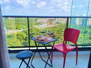 Ein Balkon mit Tisch für zwei Personen, einem roten Stuhl und Blick auf eine Stadtlandschaft und Grünflächen.