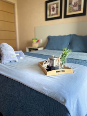 A neatly made bed with a tray containing a coffee pot and a small plant, a nightstand with a box of tissues, and a wall with framed pictures. - Cozy 1-bedroom apartment with AC in beautiful São Luís (São Luís)