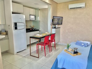 Una camera d'albergo compatta con angolo cottura, una zona pranzo con sedie rosse, un letto con copriletto blu e una TV a parete.