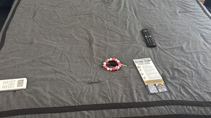 En säng med ett grått överkast, en fjärrkontroll, en armbandsur och en lapp på sängen.