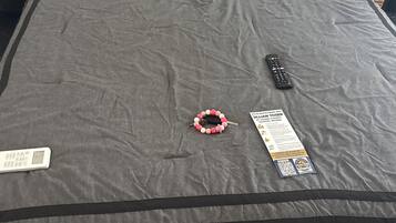 A bed with a grey bedspread, a remote control, a wristwatch, and a note on the bed.