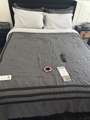 A bed with a grey bedspread, a remote control, a wristwatch, and a note on the bed. - Surf Escape: Cozy 1-bedroom studio in tranquil Ponte Vedra Beach FL with AC (Palm Valley)