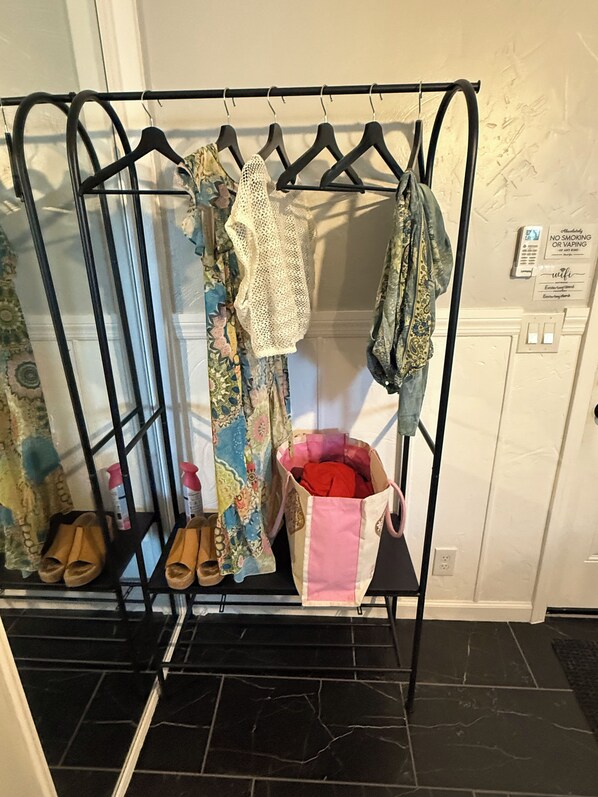 Un portant à vêtements avec divers articles d’habillement et des chaussures, un sac contenant des objets rouges, et un panneau indiquant qu’il est interdit de fumer ou de vapoter.