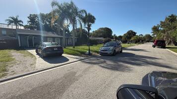 A residential street with houses, parked cars, and palm trees.