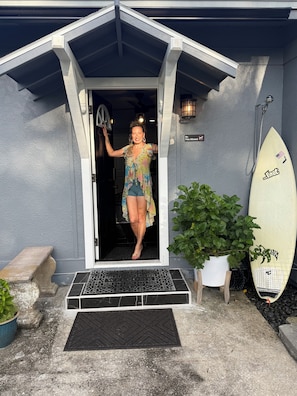 Une personne entre dans un bâtiment, une planche de surf à la main et un paillasson devant la porte.