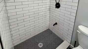 A shower with white subway tiles, a black showerhead, and a white toilet.