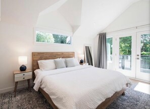 A bedroom with a large bed, a nightstand, a window, and a view of greenery. - 2-bedroom coach house in welcoming North Vancouver with AC (North Vancouver)