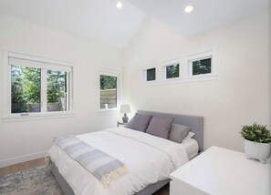 A bedroom with a bed, bedside table, lamp, and a potted plant. - 2-bedroom coach house in welcoming North Vancouver with AC (North Vancouver)