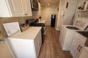 A narrow kitchen with white cabinets, a stove, and a refrigerator. - Cozy Private Casita Near RUHS with Full Kitchen, Laundry and Parking (Moreno Valley)