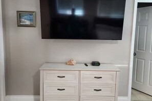 A room with a white dresser, a flat-screen TV mounted on the wall, and a framed picture on the wall. - Cozy Private Casita Near RUHS with Full Kitchen, Laundry and Parking (Moreno Valley)