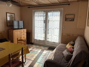 Ein Zimmer mit Esstisch, einer Couch, einem Fernseher auf einer Holzkommode und einem großen Fenster mit Vorhängen.