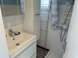 Ein Badezimmer mit einem weißen Waschbecken, einem Spiegel, einer Duschkabine und Fliesenwänden.