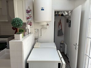 Eine kleine Küche mit weißer Arbeitsplatte, einem kleinen Topfpflanzen und einem Wasserspender.
