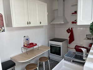 Cocina compacta con armarios blancos, estufa, lavaplatos y un pequeño mostrador con taburetes.