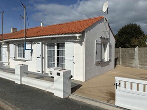 Un edificio blanco con techo de tejas rojas, antena parabólica y entrada protegida por una reja.