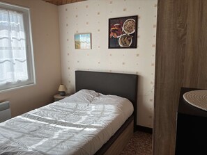 Une chambre à coucher comprenant un lit, une table de chevet, une lampe et un mur recouvert d’un papier peint à motifs, ainsi que deux tableaux encadrés.