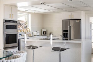 A modern kitchen with stainless steel appliances, a glass island, and bar stools. - ZAINALAND!! Mythic Desert Den!! (Twentynine Palms)