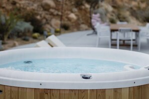 Ein Whirlpool auf Holzunterlage, umgeben von Gartenmöbeln und einer felsigen Landschaft.