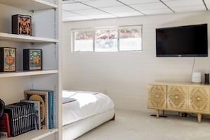 Une chambre à coucher avec un lit, un téléviseur fixé au mur, une bibliothèque remplie de livres et une fenêtre donnant sur un beau paysage.