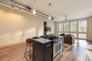 Eine moderne Küche mit einer zentralen Kochinsel, einem Essbereich mit brauner Ledersofa und großen Fenstern, die für natürliches Licht sorgen.