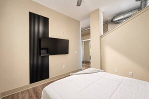 Ein modernes Hotelzimmer mit einem Bett, einem an der Wand befestigten Fernseher und freiliegenden Lüftungsrohren an der Decke.